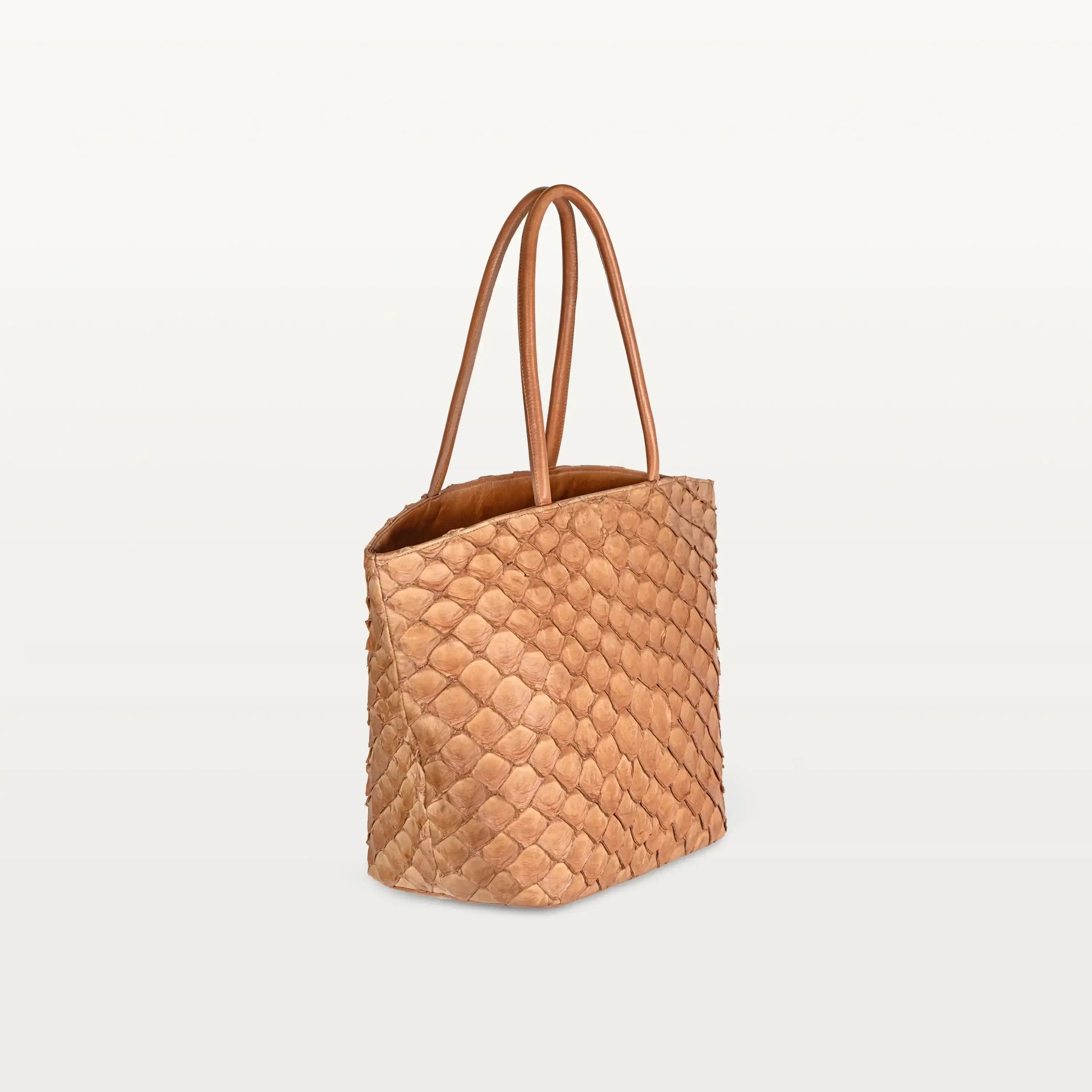 Side view of the spacious Delray Shopper in cognac pirarucu leather, a large tote bag with a unique fish scale texture and two top handles.