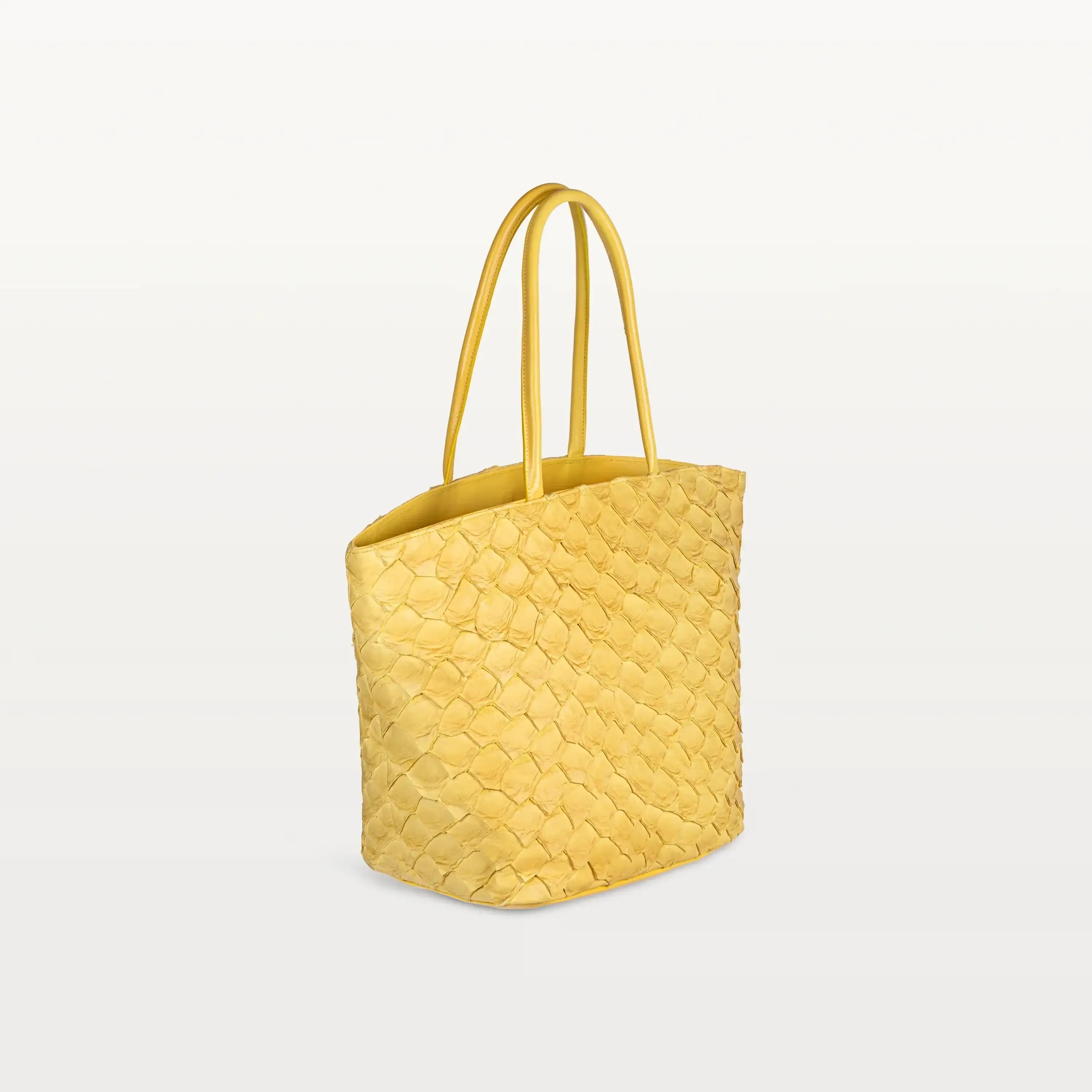 Side view of the spacious Delray Shopper in honey yellow pirarucu leather, a large tote bag with a unique fish scale texture and two top handles.