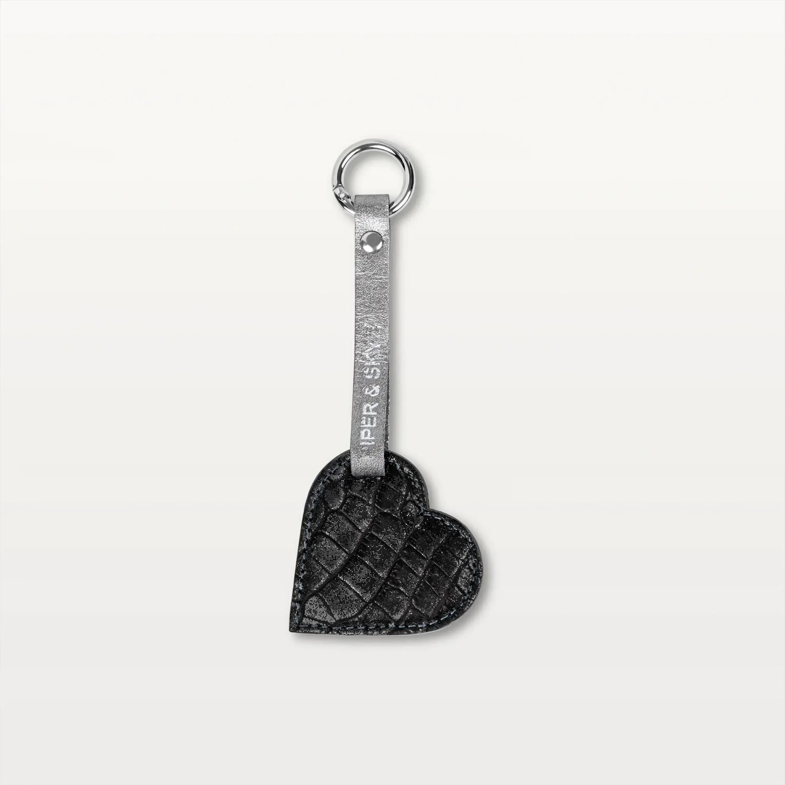 A heart-shaped keychain made from metallic grey alligator leather hanging from a thin leather strap with a silver metallic ring.