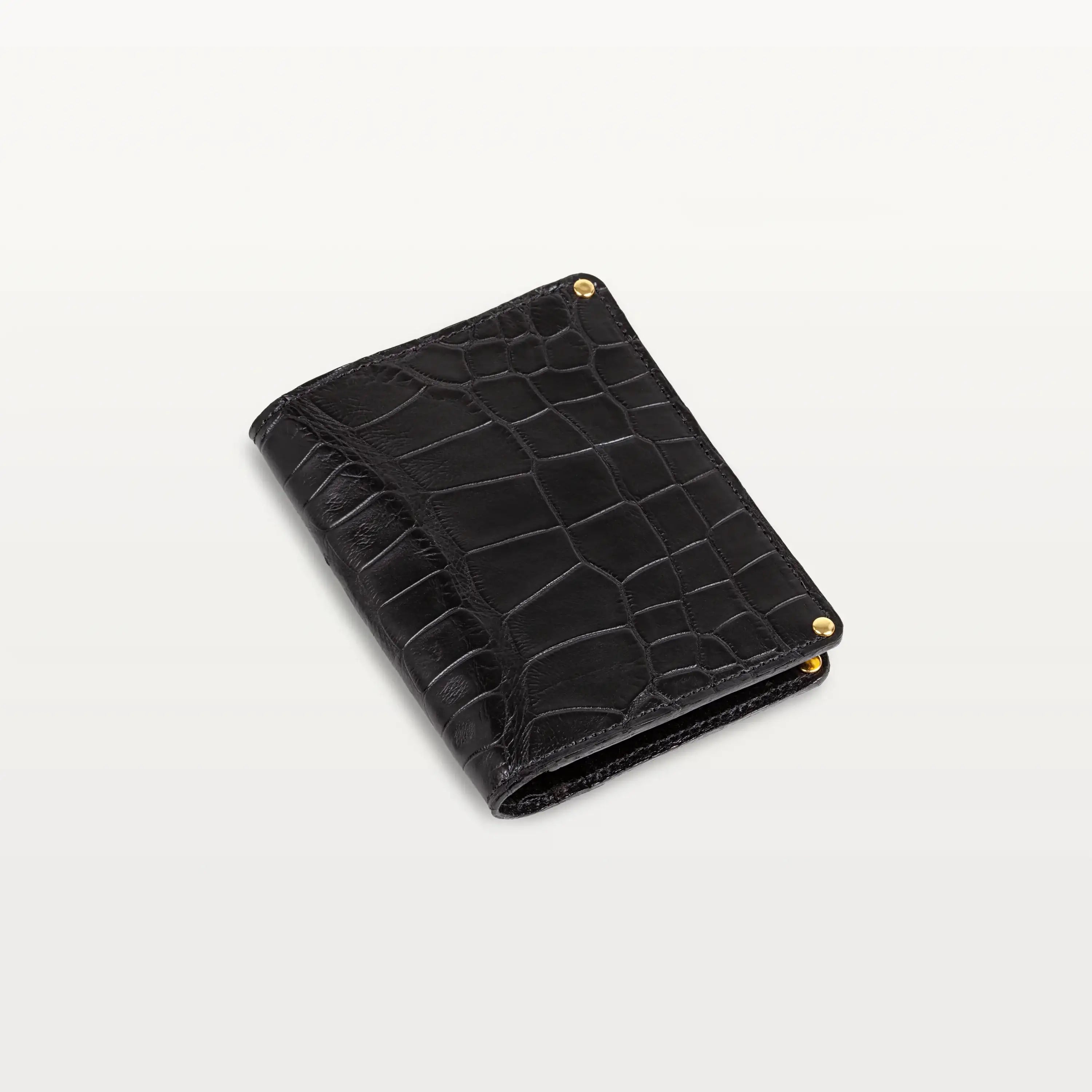 A closed passport holder made of glossy black alligator leather with gold rivets.