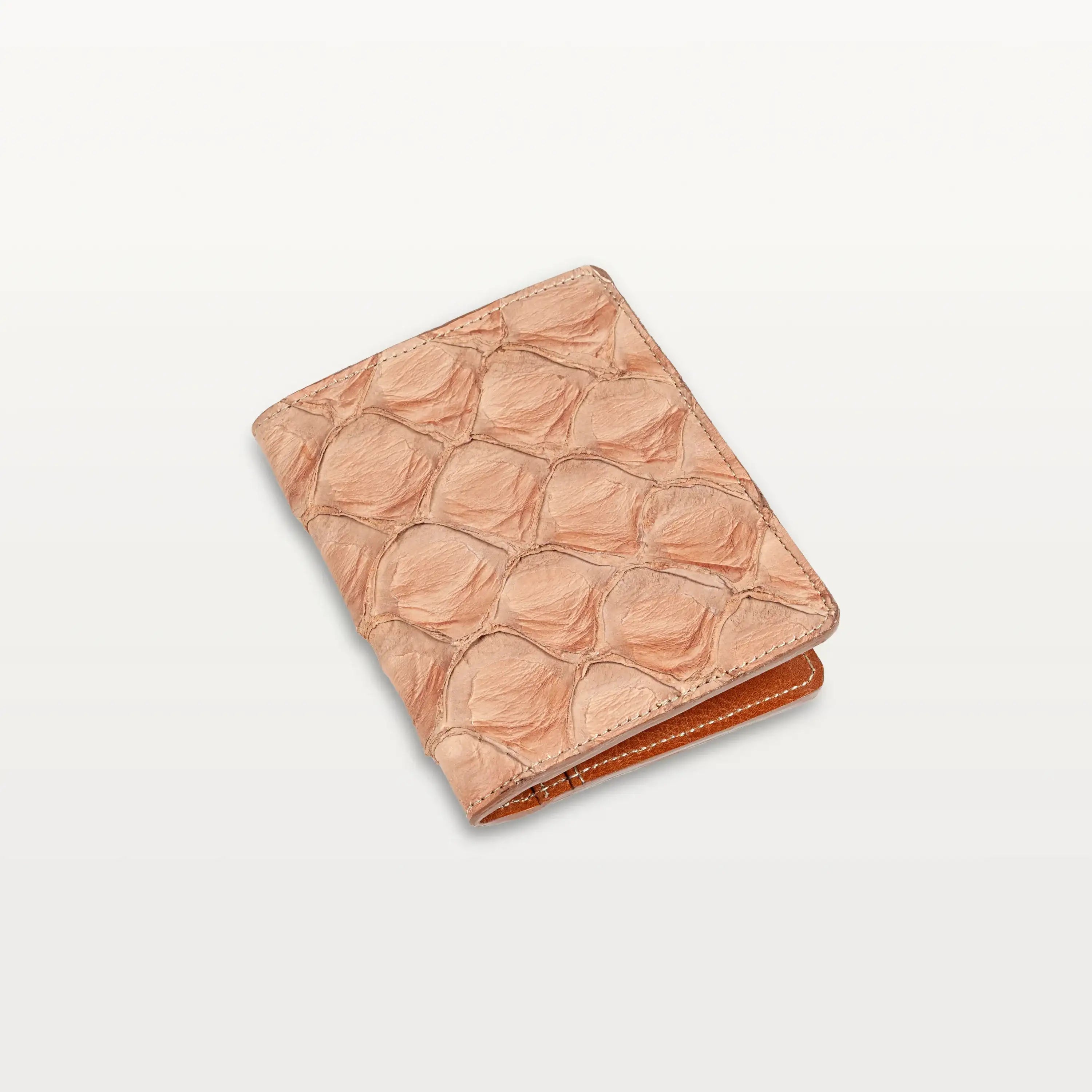 A closed passport holder made of cognac colored Pirarucu fish leather with a distinct, textured scale pattern