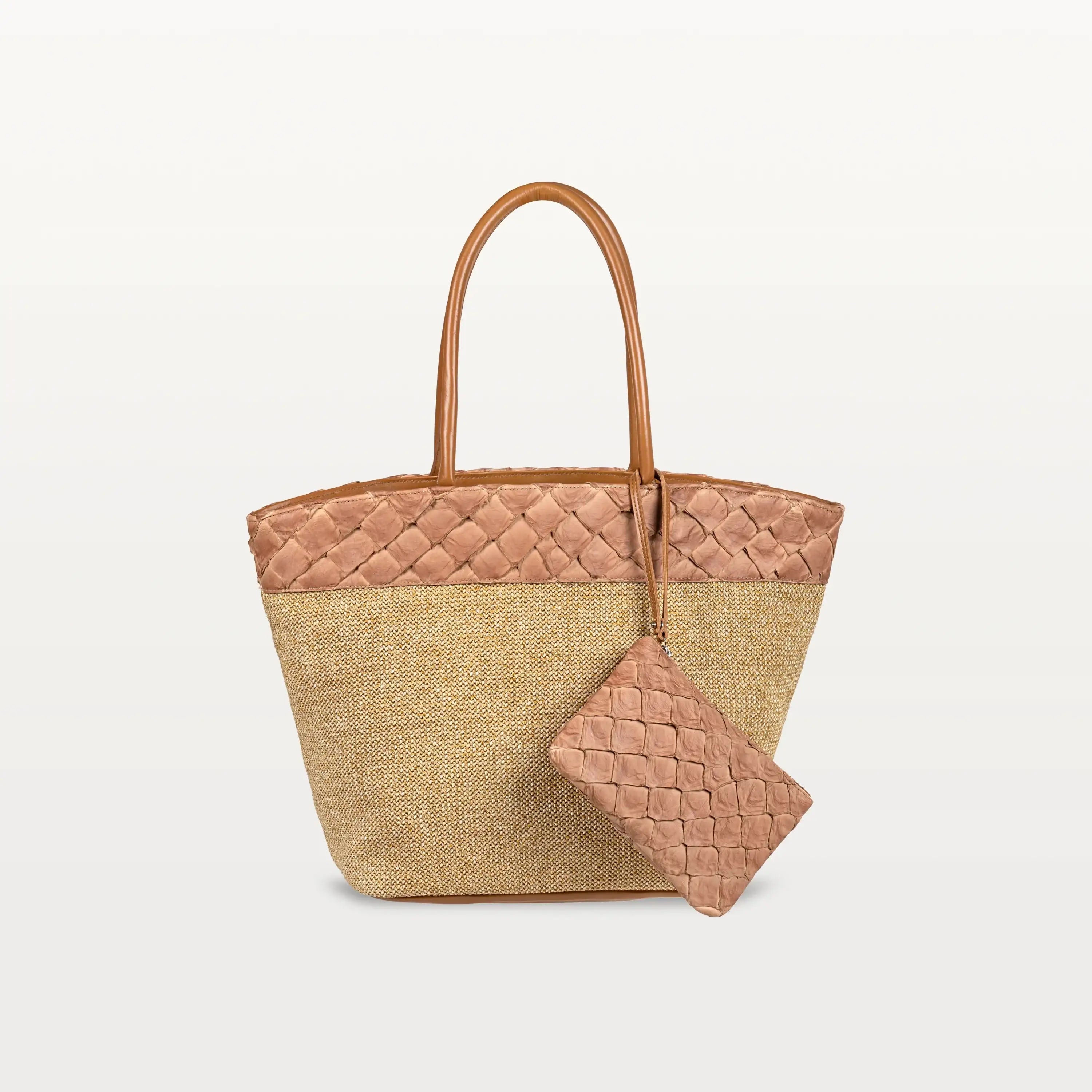 The Rio Beach Bag with a camel raffia body and cognac pirarucu leather trim. A matching cognac pirarucu leather wristlet hangs from the strap