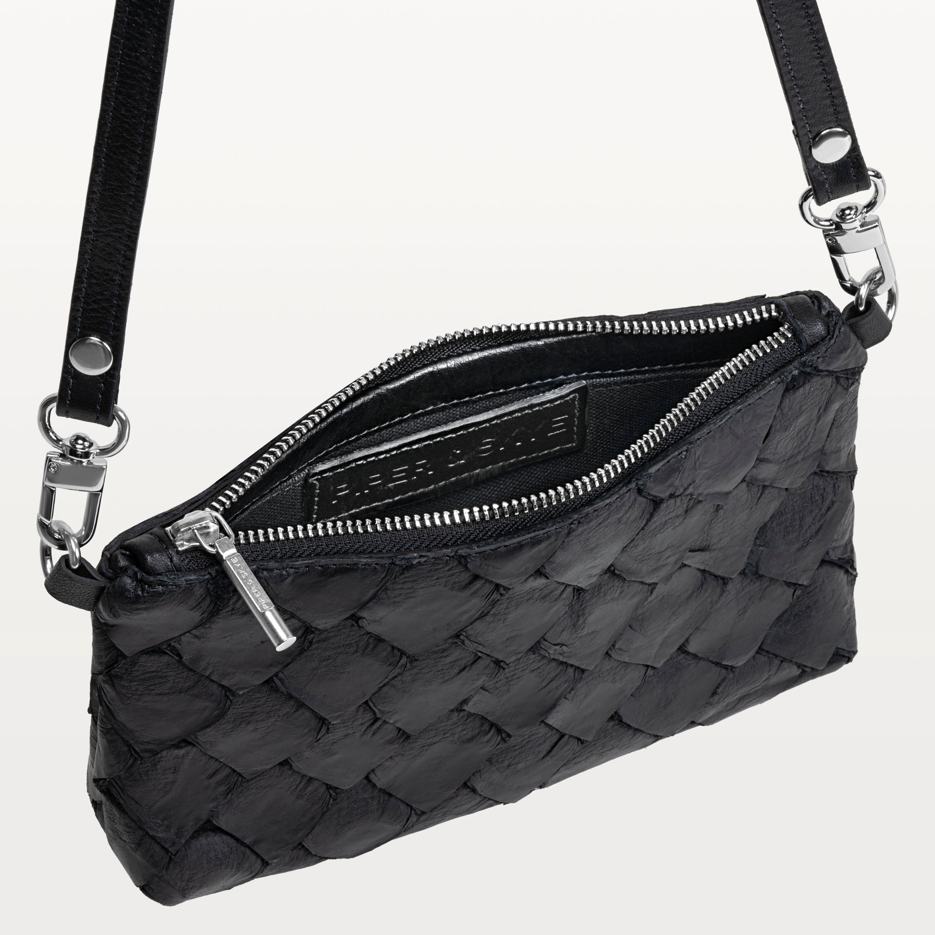 Black crossbody bag made of pirarucu leather with its silver zipper open revealing the Piper & Skye logo inside. 