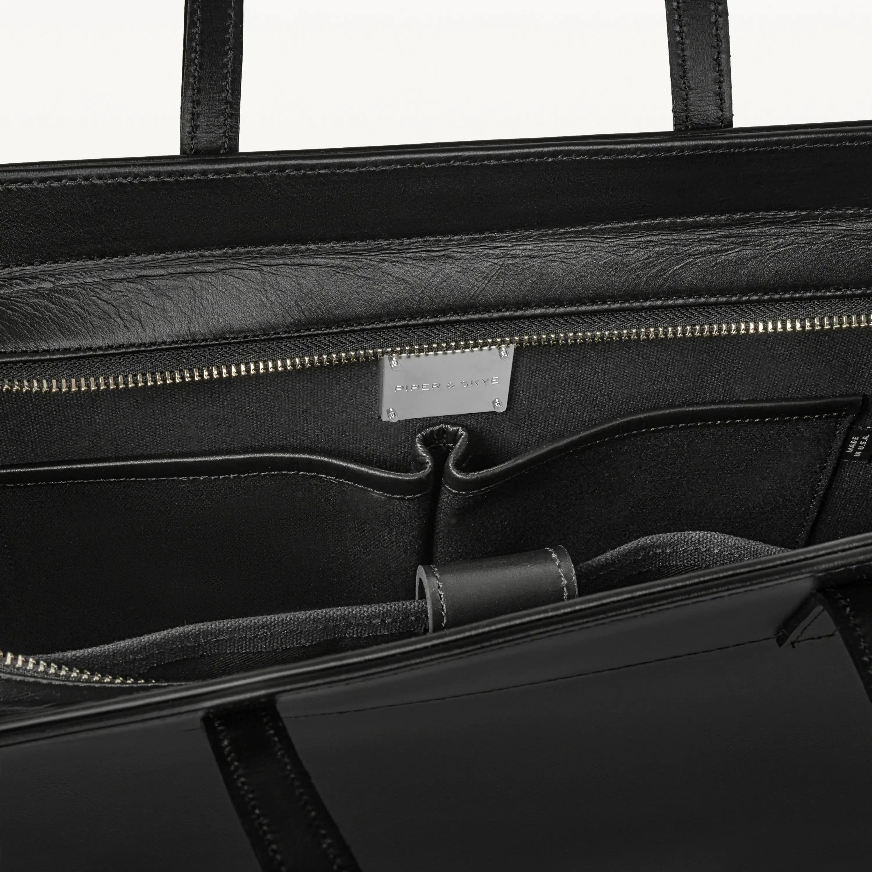 Top zipper of the Braemar tote bag in black pirarucu leather open to show the inner laptop sleeve. 