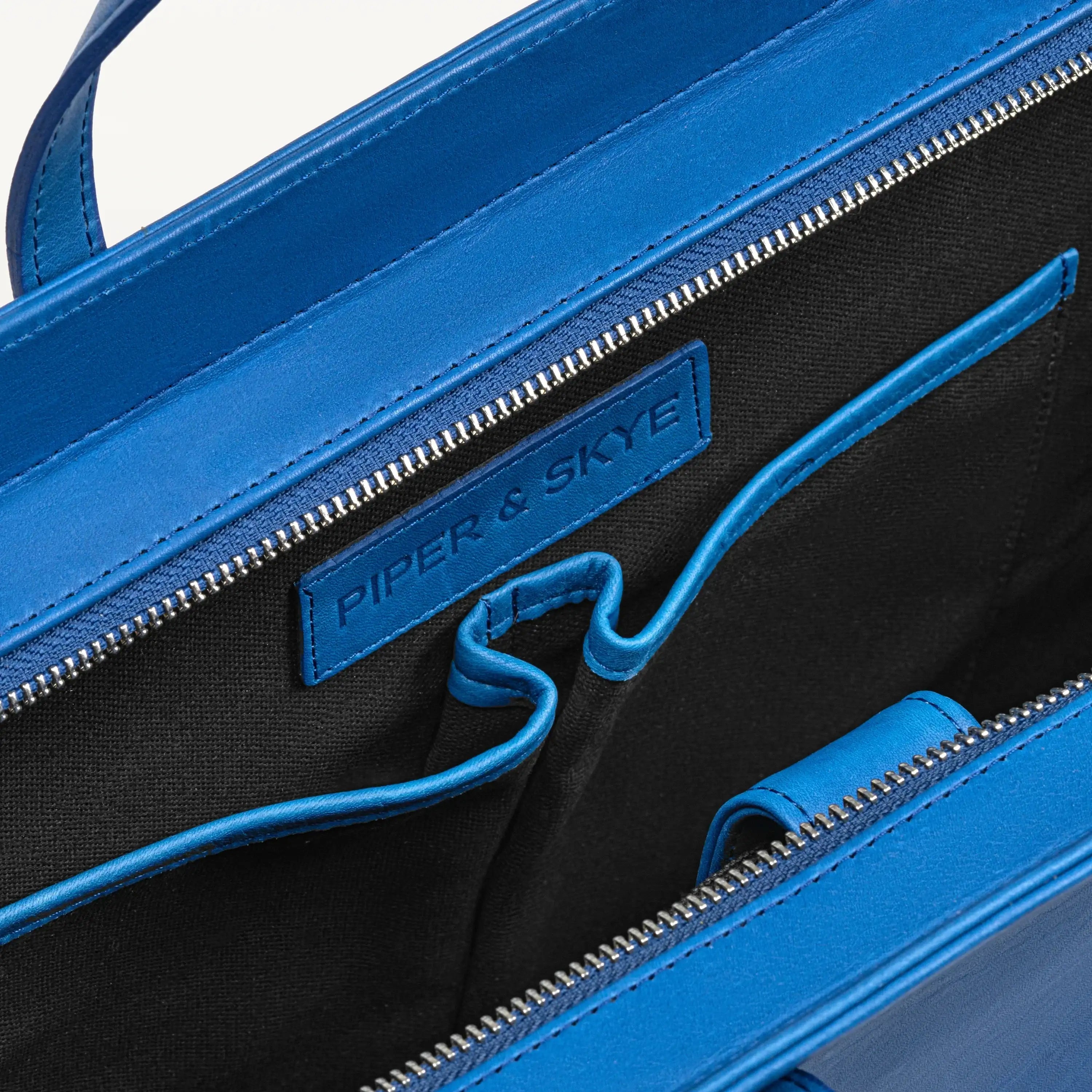 Top zipper of the Braemar tote bag in cobalt blue pirarucu leather open to show the inner laptop sleeve. 