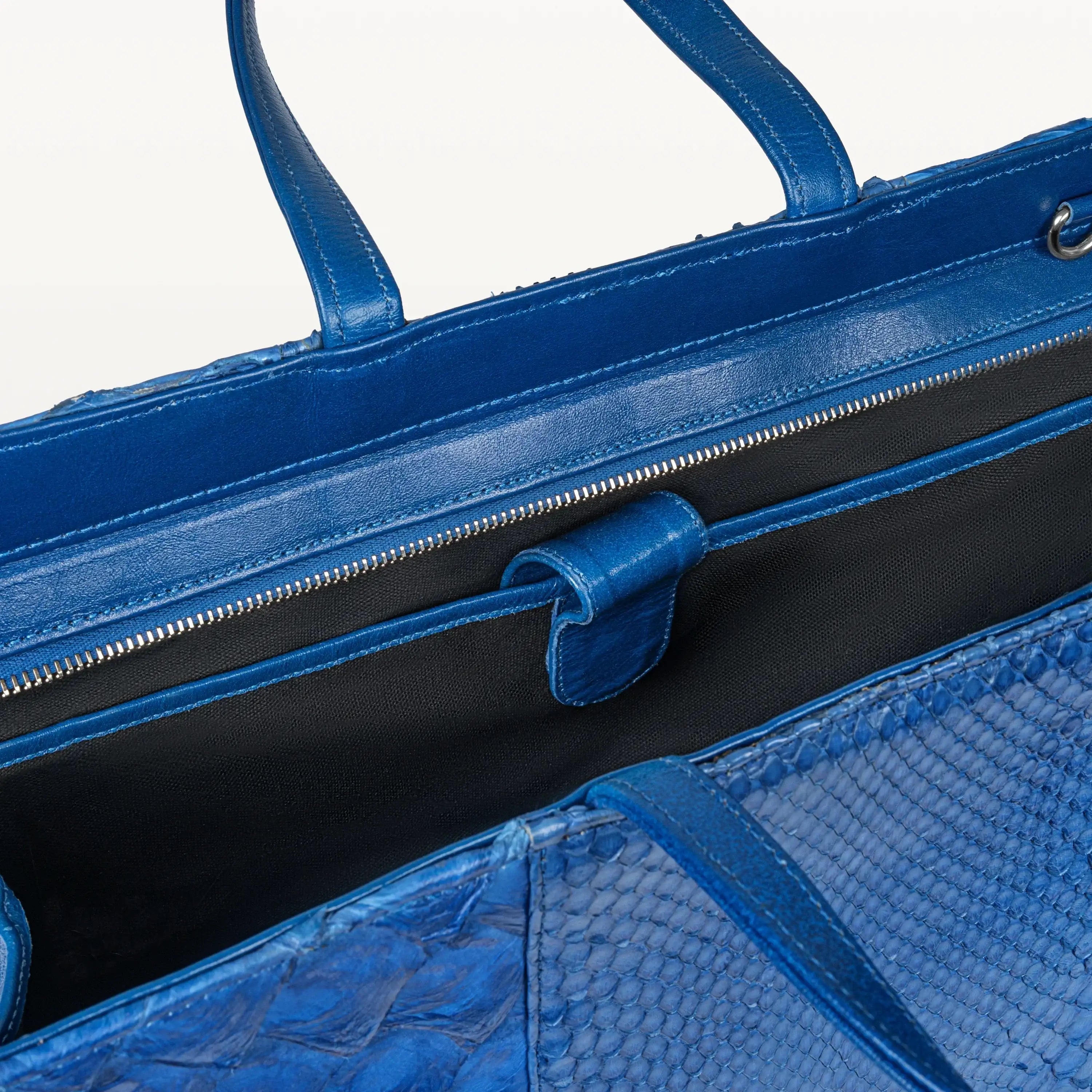 Top zipper of the Braemar tote bag in cobalt blue python and pirarucu leather open to show the inner laptop sleeve. 