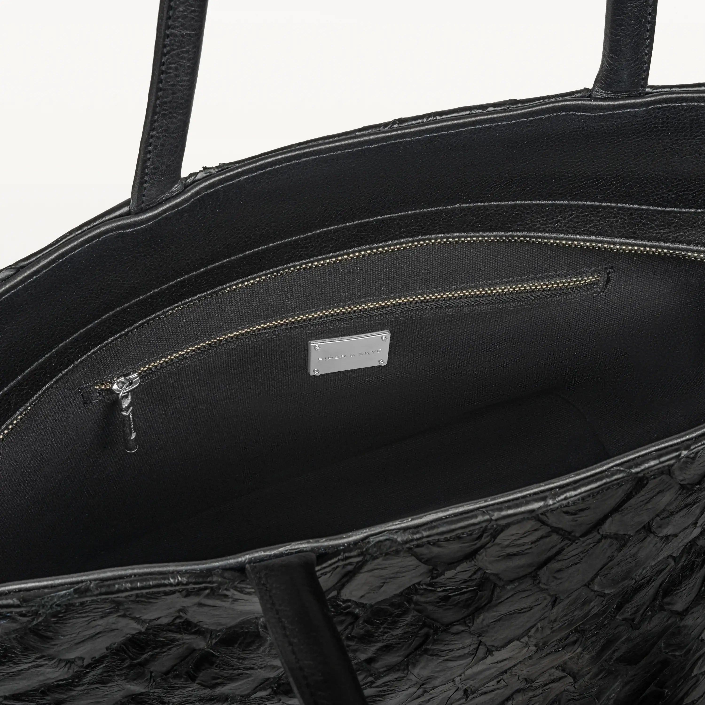Delray shopper tote bag in black pirarucu leather opened to show the black interior lining and inner zipper pocket. 