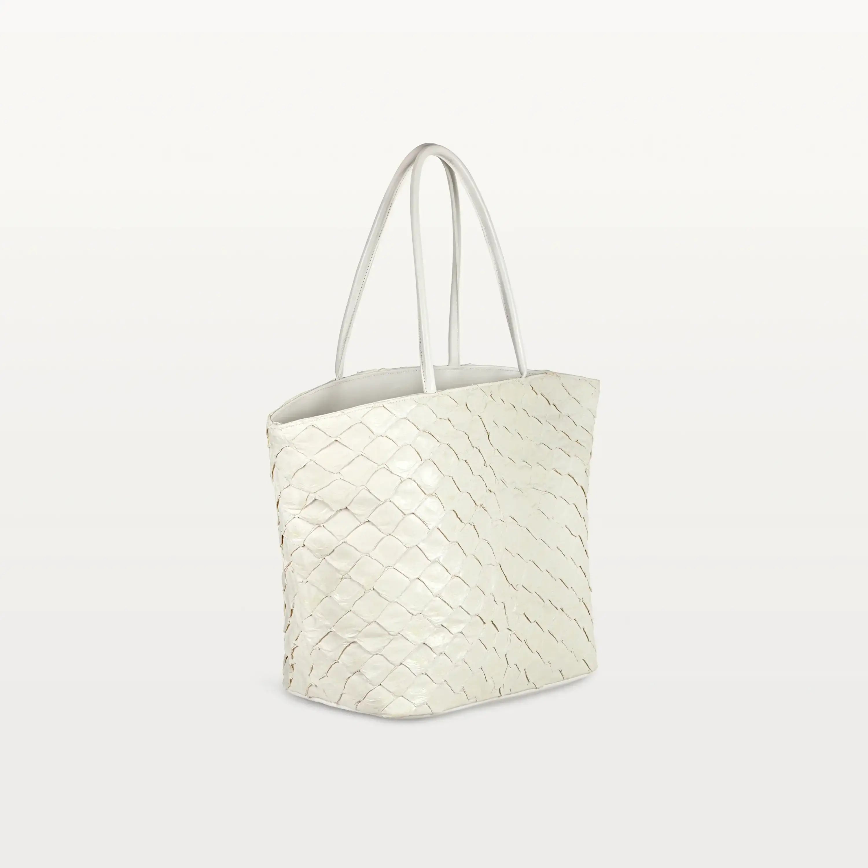 Side view of the spacious Delray Shopper in clay white pirarucu leather, a large tote bag with a unique fish scale texture and two top handles. 