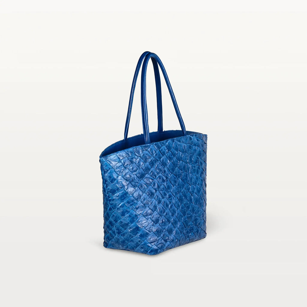 Side view of the spacious Delray Shopper in cobalt blue pirarucu leather, a large tote bag with a unique fish scale texture and two top handles. 