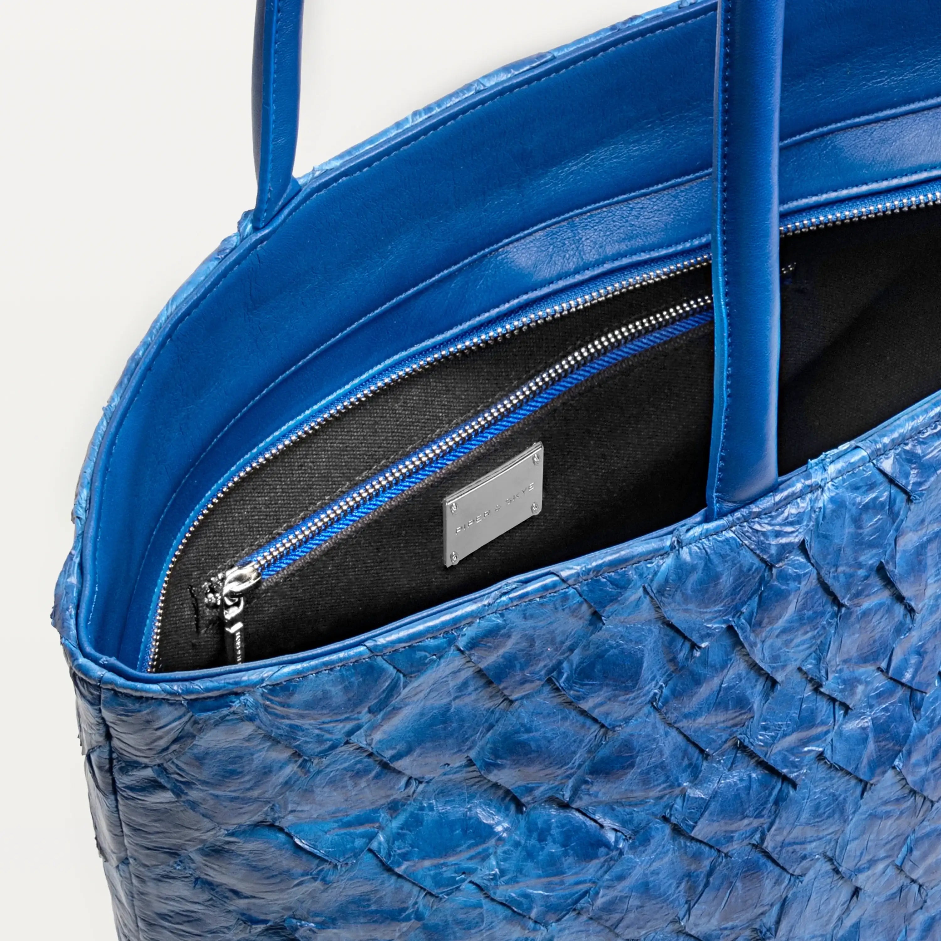 Delray shopper tote bag in cobalt blue pirarucu leather opened to show the black interior lining and inner zipper pocket. 
