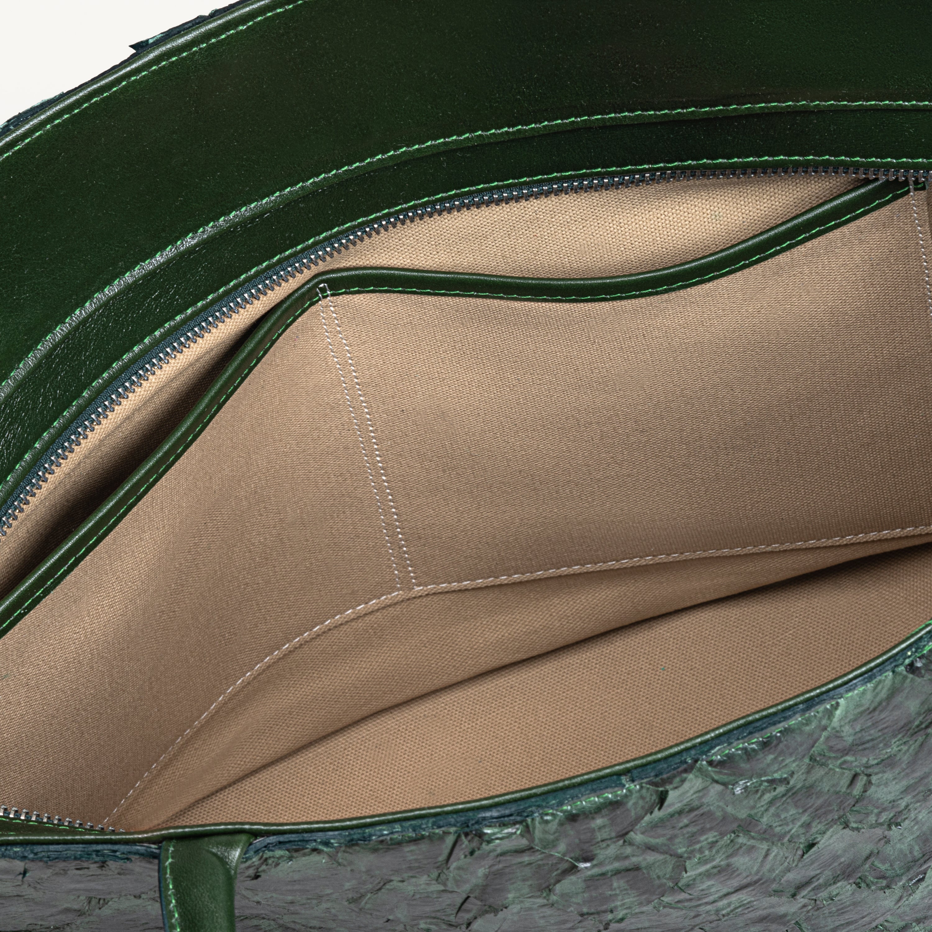 Top zipper of the verdant green Delray tote bag opened to show the beige interior lining and two inner slip pockets. 