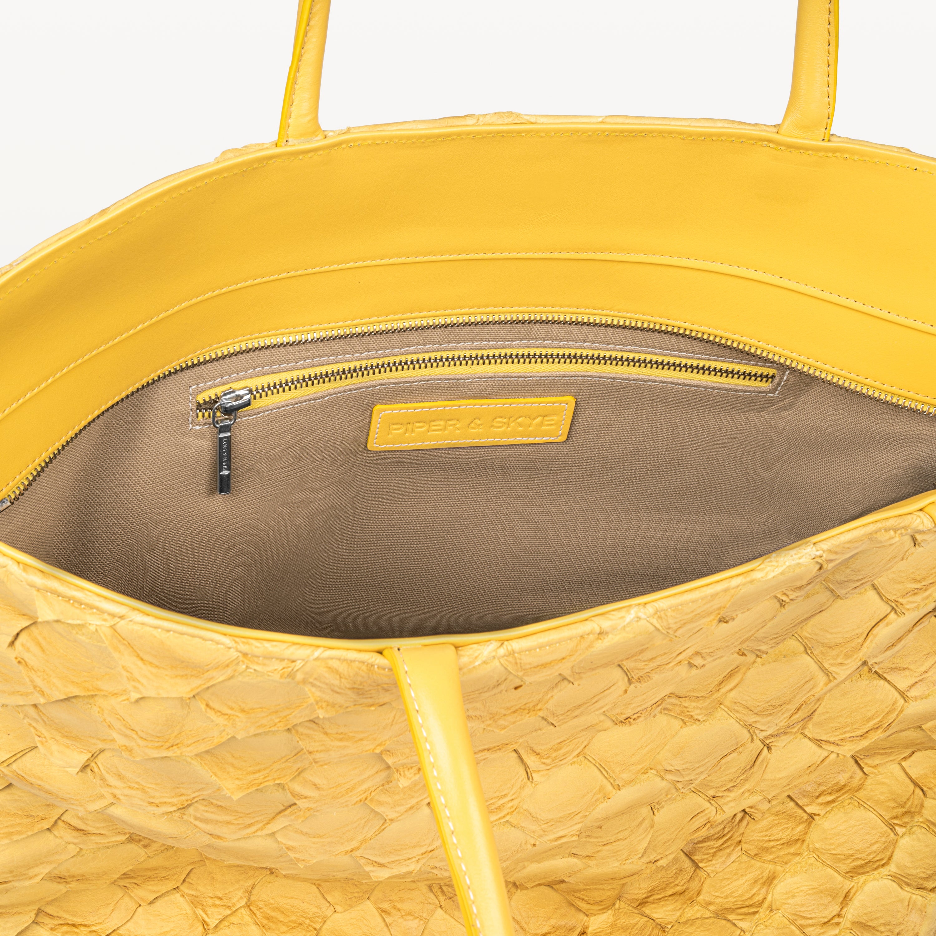 Delray shopper tote bag in honey yellow pirarucu leather opened to show the beige interior lining and inner zipper pocket. 