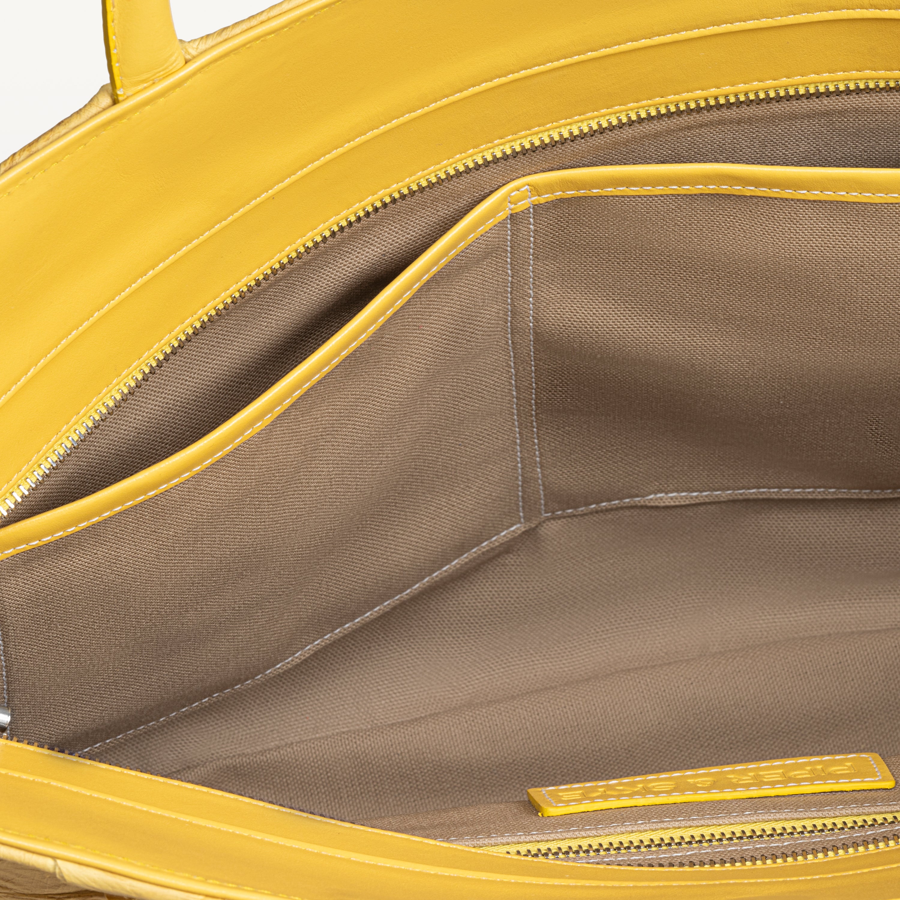Top zipper of the honey yellow Delray tote bag opened to show the beige interior lining and two inner slip pockets. 