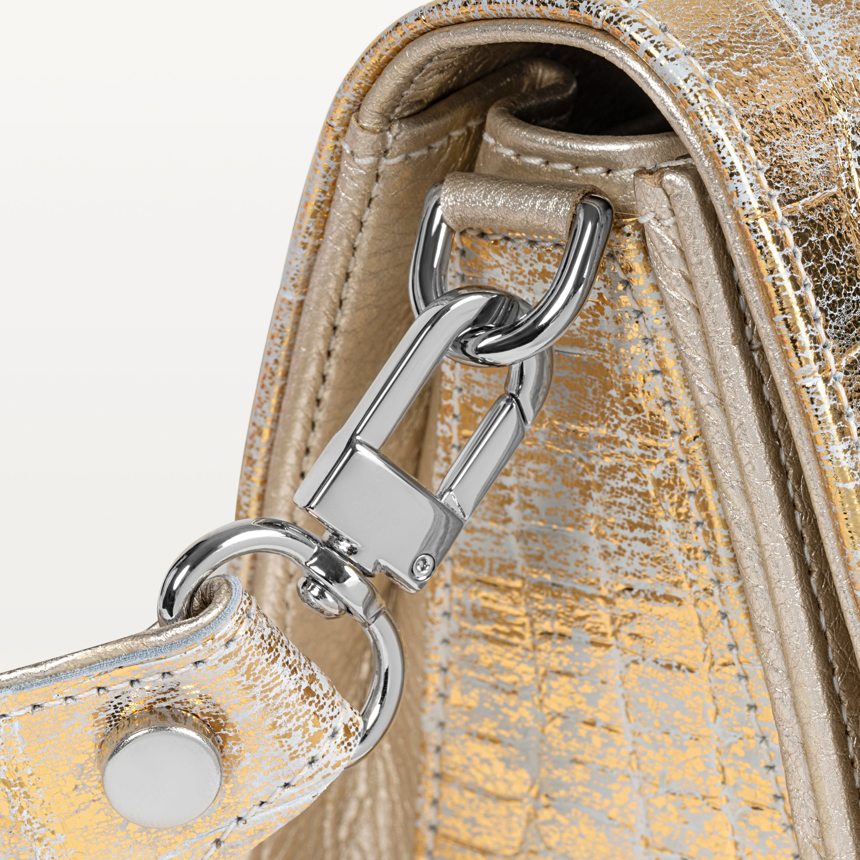 Close up view of the side gusset of the metallic gold Lola crossbody bag in alligator along with the silver D-ring and crossbody strap attachment. 