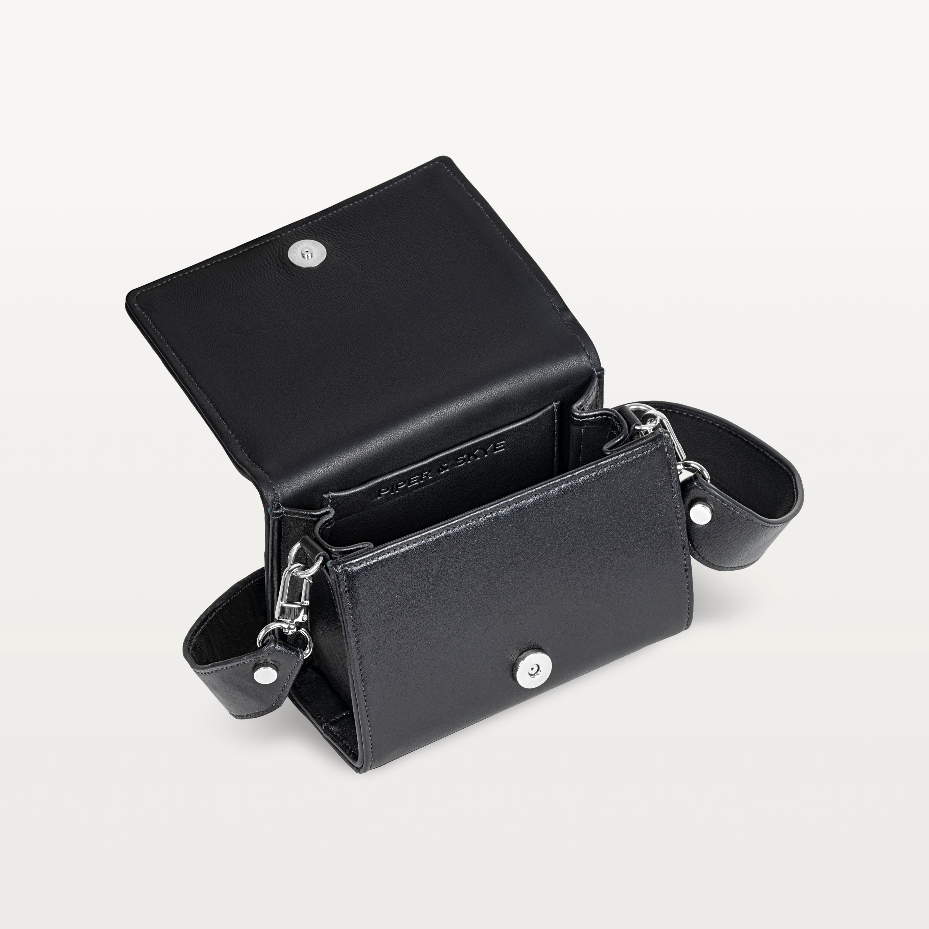 Interior view, with the front flap lifted, of the black pirarucu Lola crossbody bag showing the magnetic snap closure and inner pocket. 