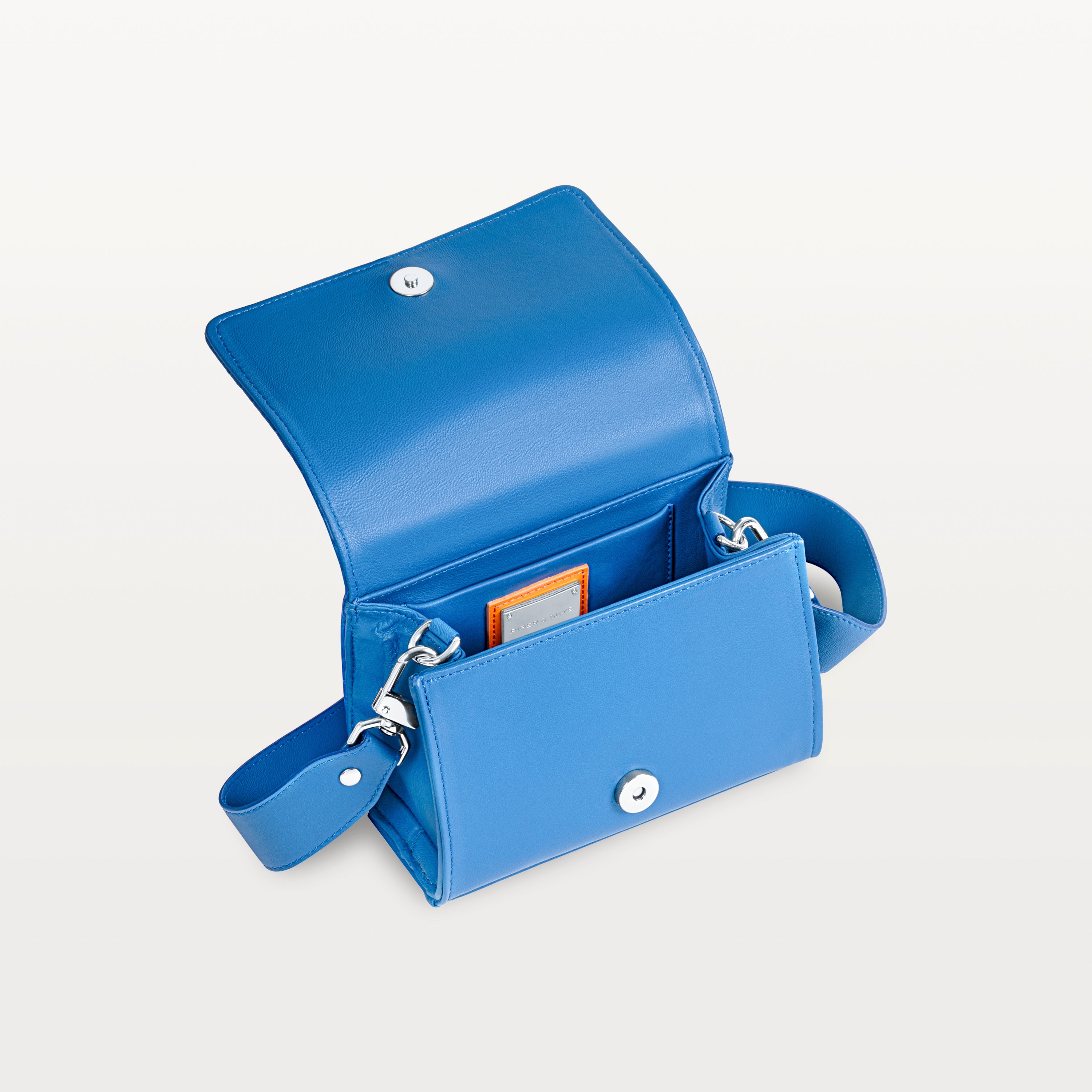 Interior view, with the front flap lifted, of the cobalt blue pirarucu Lola crossbody bag showing the magnetic snap closure and inner pocket. 