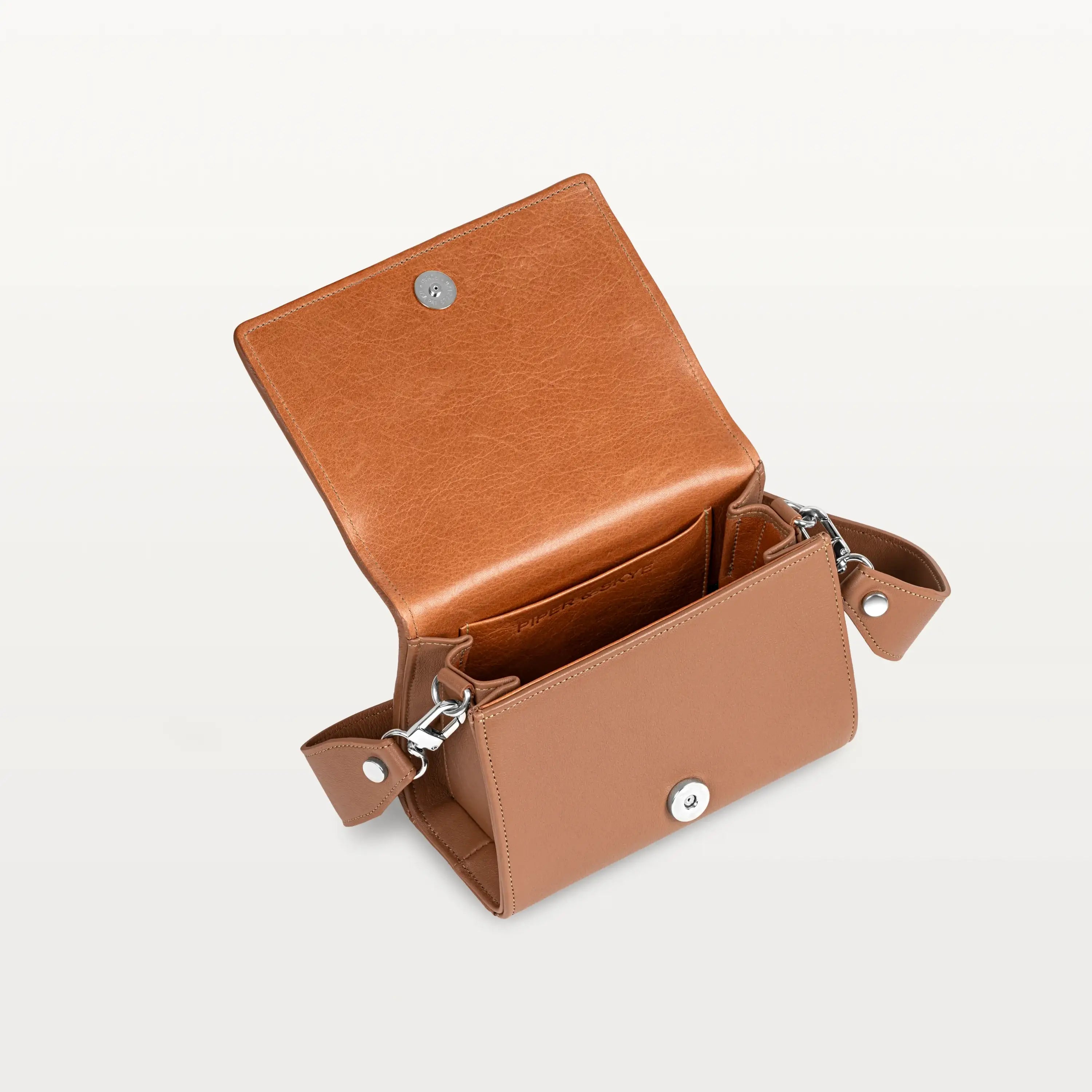 Interior view, with the front flap lifted, of the cognac pirarucu Lola crossbody bag showing the magnetic snap closure and inner pocket. 