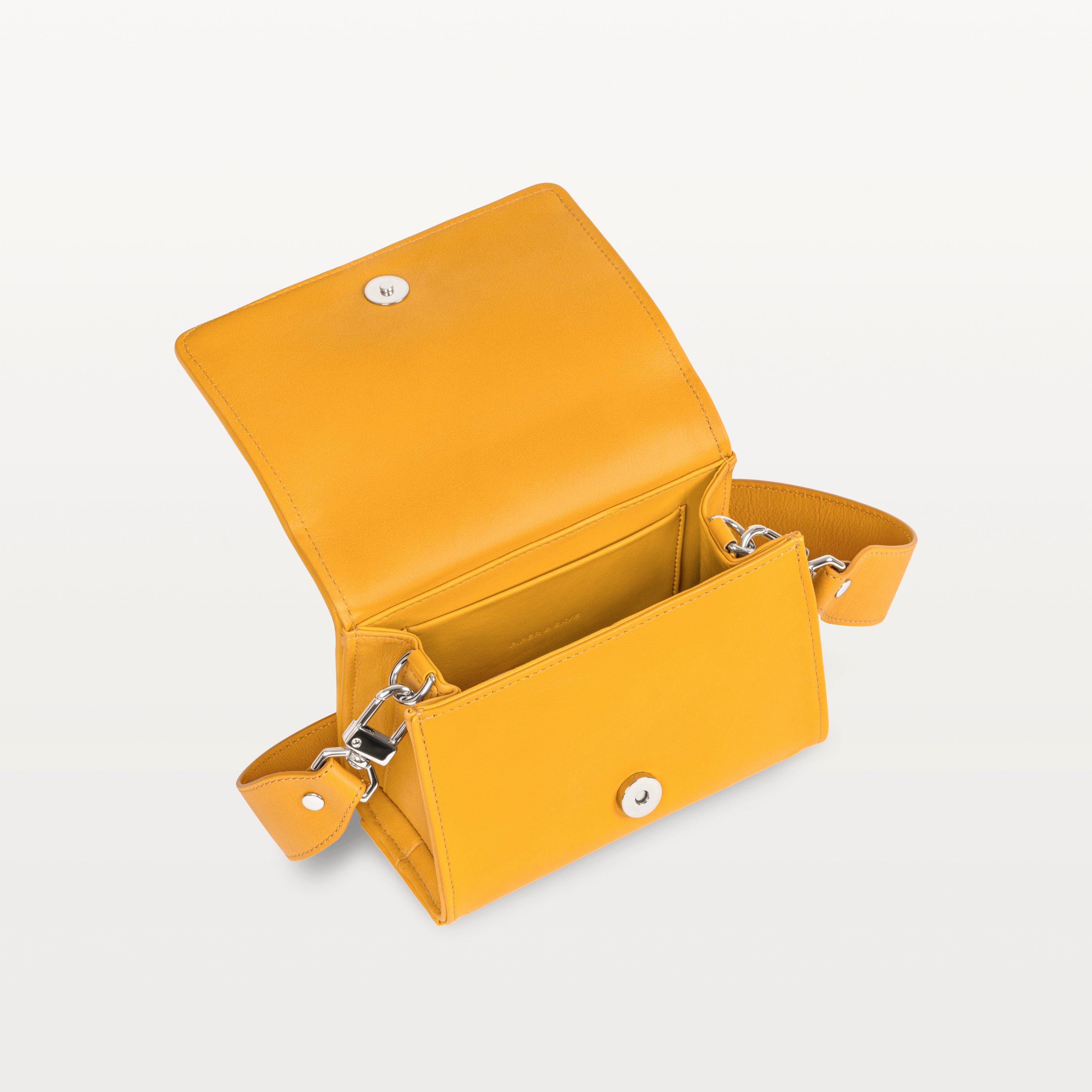 Interior view, with the front flap lifted, of the honey yellow pirarucu Lola crossbody bag showing the magnetic snap closure and inner pocket. 