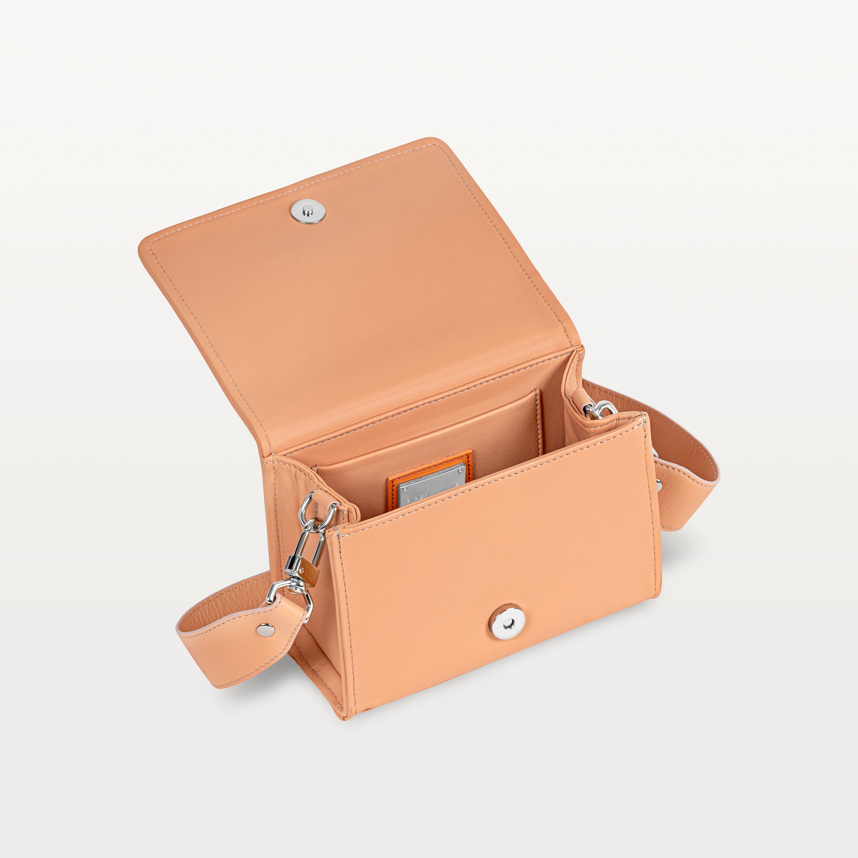 Interior view, with the front flap lifted, of the pink pirarucu Lola crossbody bag showing the magnetic snap closure and inner pocket. 