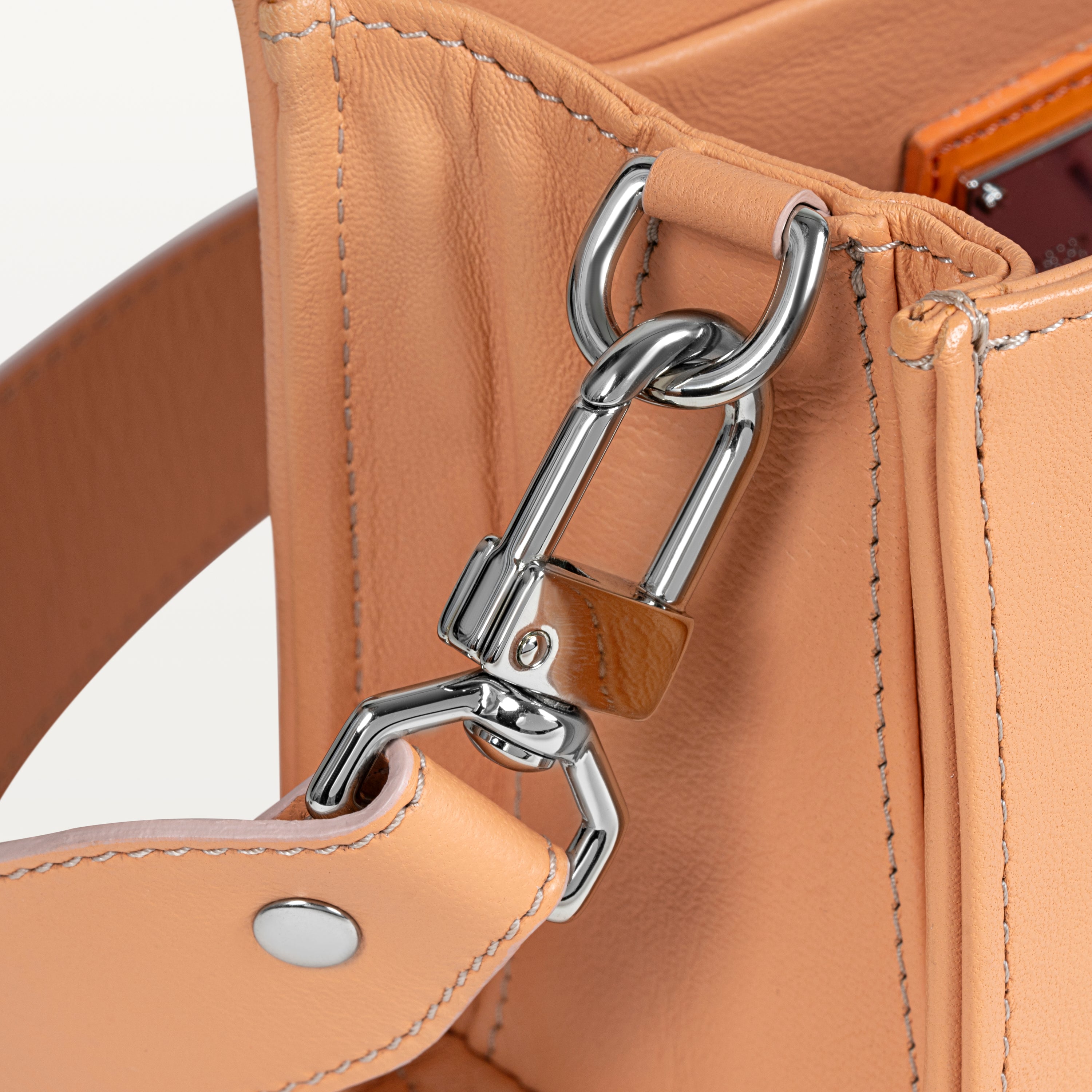 Close up view of the side gusset of the pink Lola crossbody bag in pirarucu fish leather along with the silver D-ring and crossbody strap attachment. 