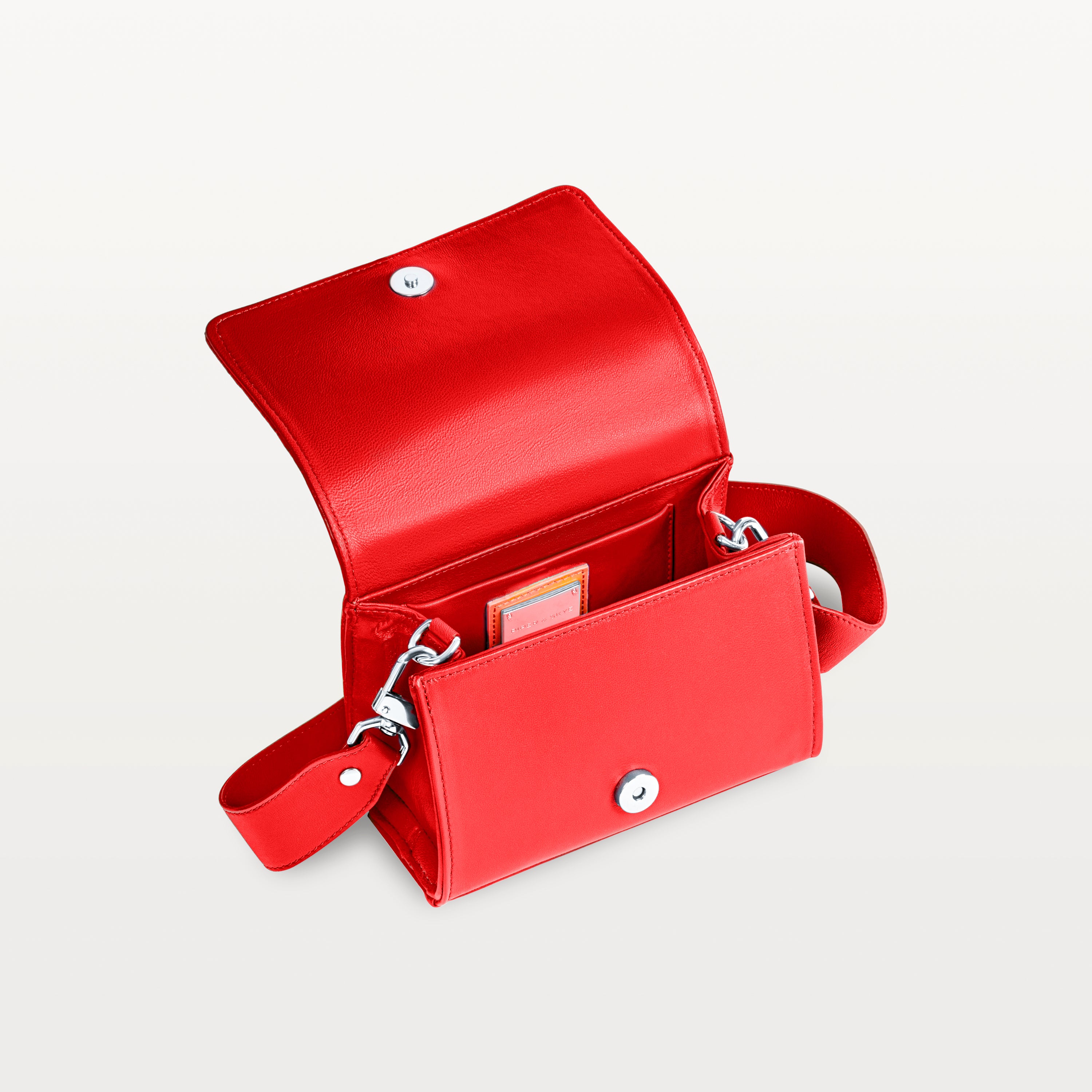 Interior view, with the front flap lifted, of the red pirarucu Lola crossbody bag showing the magnetic snap closure and inner pocket. 