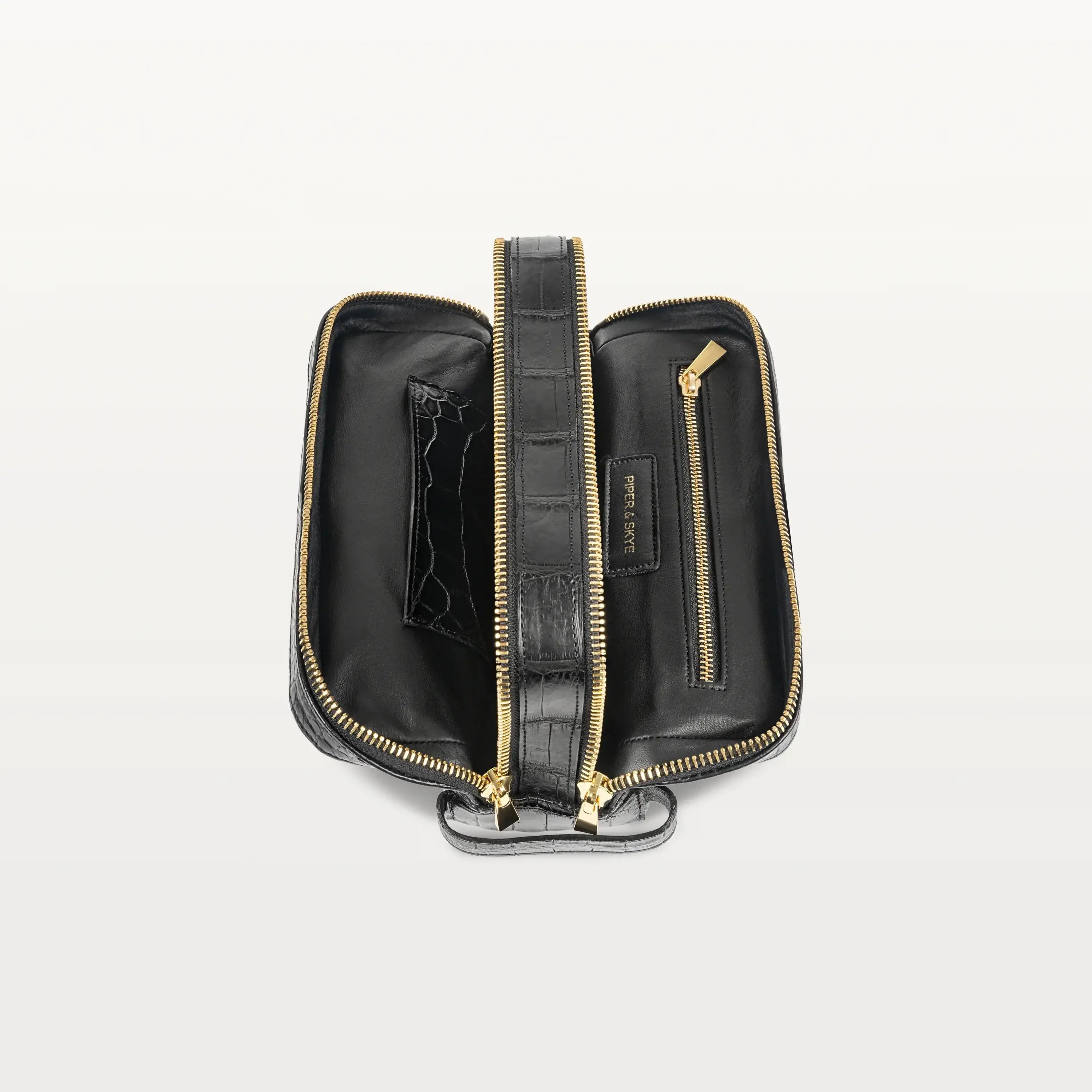 Both gold-zippered compartments of the Nomad Dopp Kit in black alligator opened to show an interior zippered pocket on one side. 