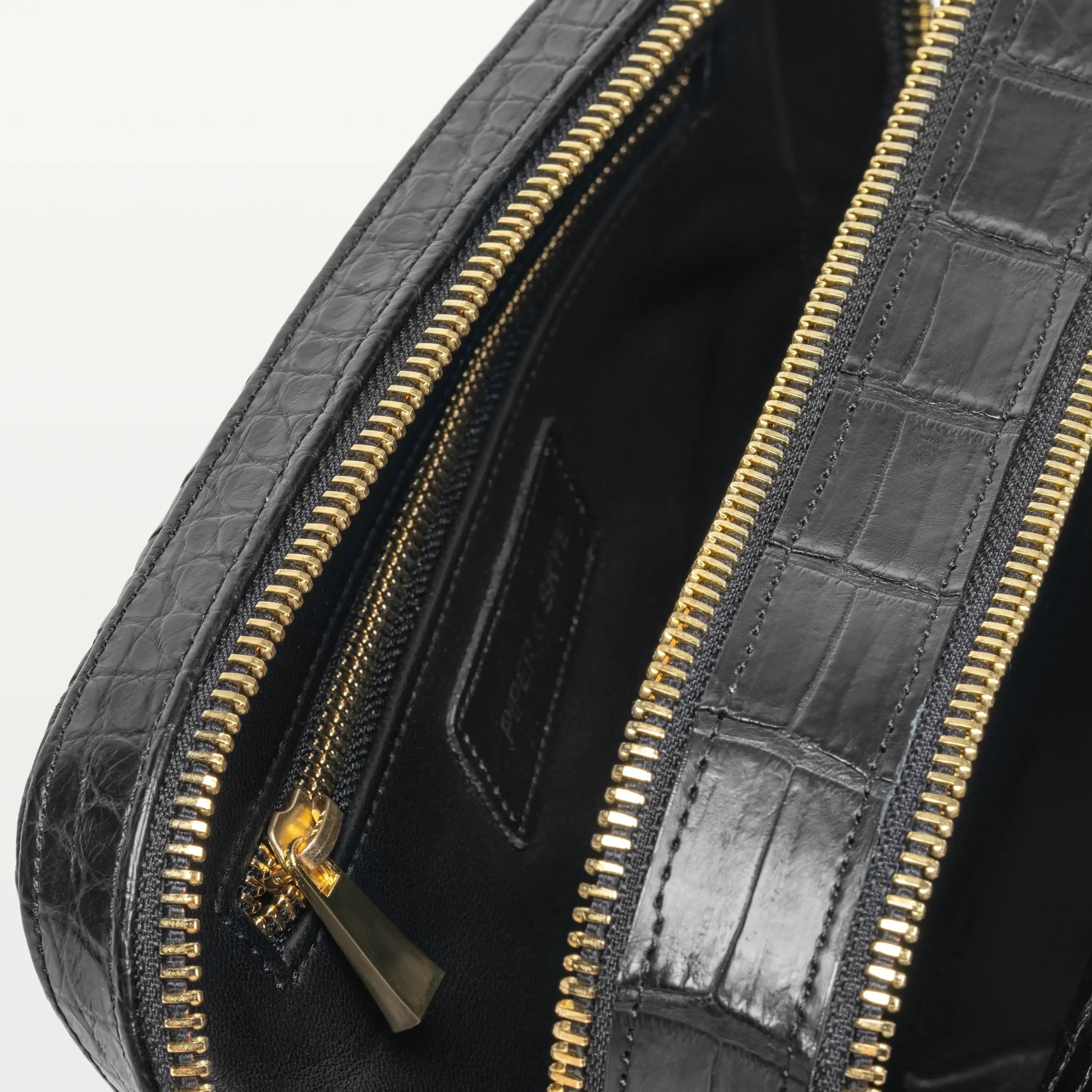 A close up view of the Nomad Dopp Kit  opened up showing the glossy black alligator material and the gold zipper compartments. 