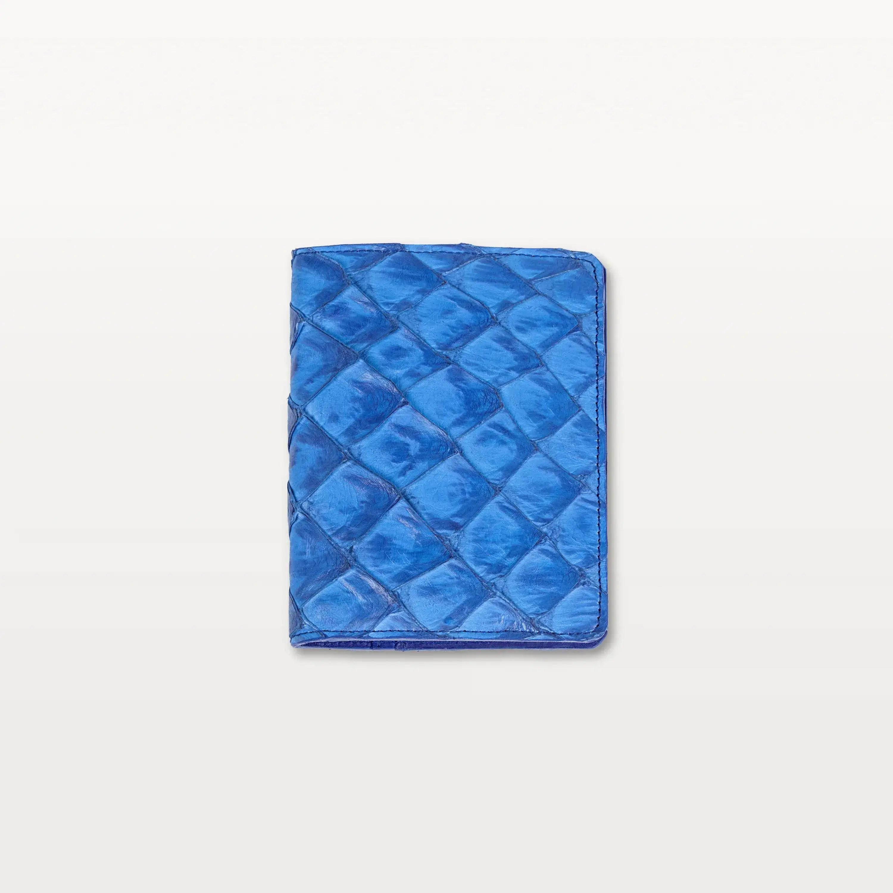 A cobalt blue passport holder with a textured fish scale pattern, made from sustainable Pirarucu leather