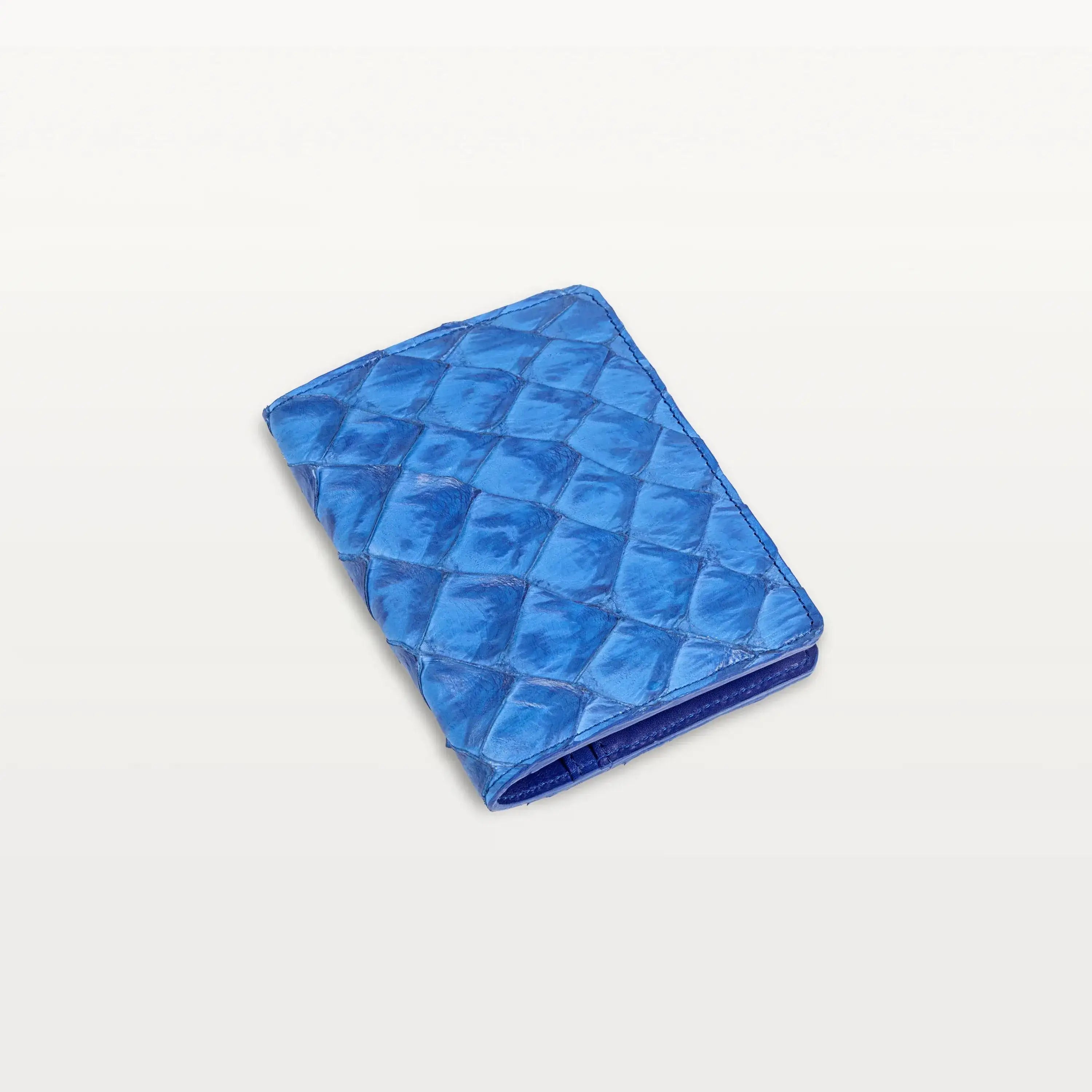 A closed passport holder made of cobalt blue colored Pirarucu fish leather with a  distinct, textured scale pattern