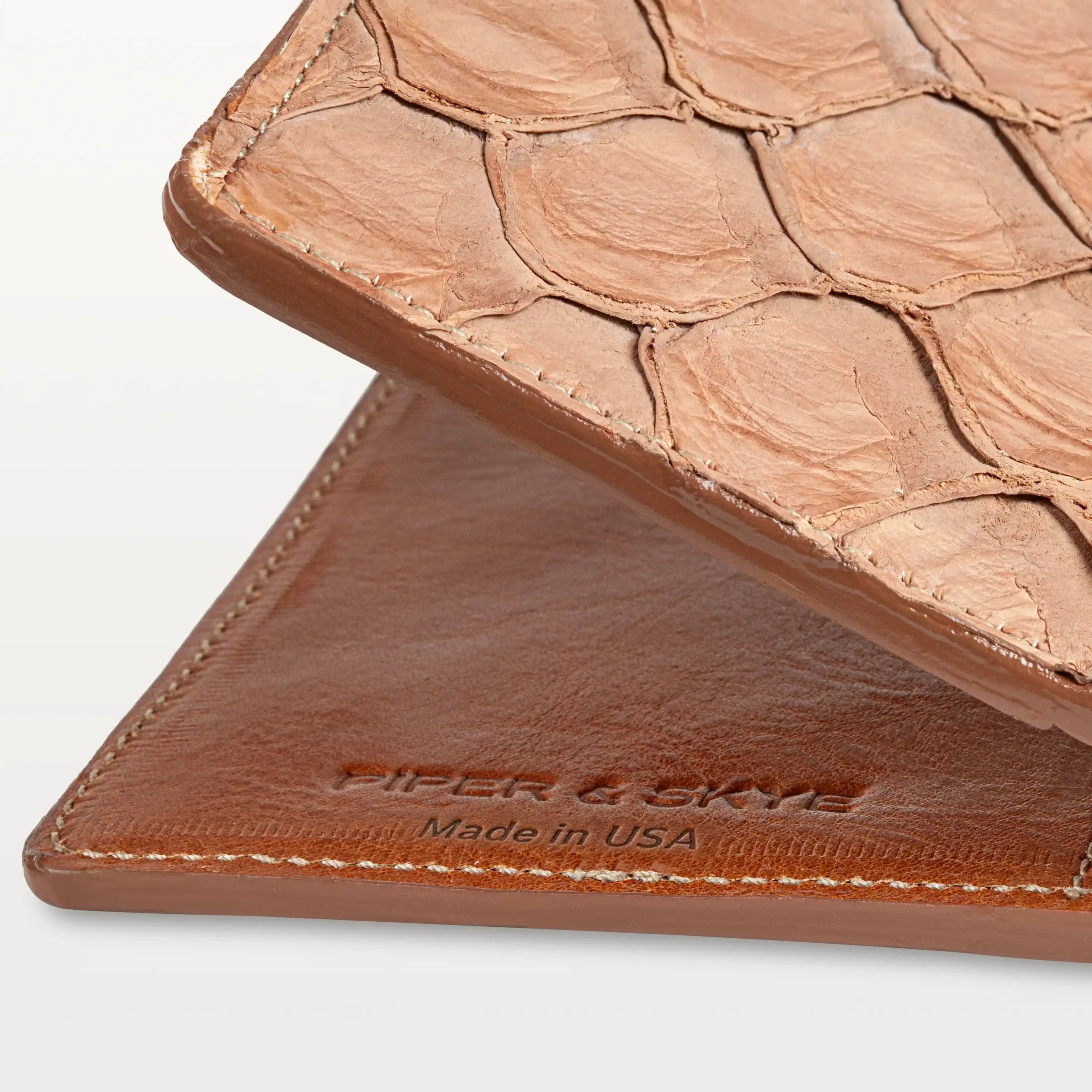 Close up view of the cognac pirarucu passport holder showing the fish scale pattern, embossed logo and 'Made in USA'. 