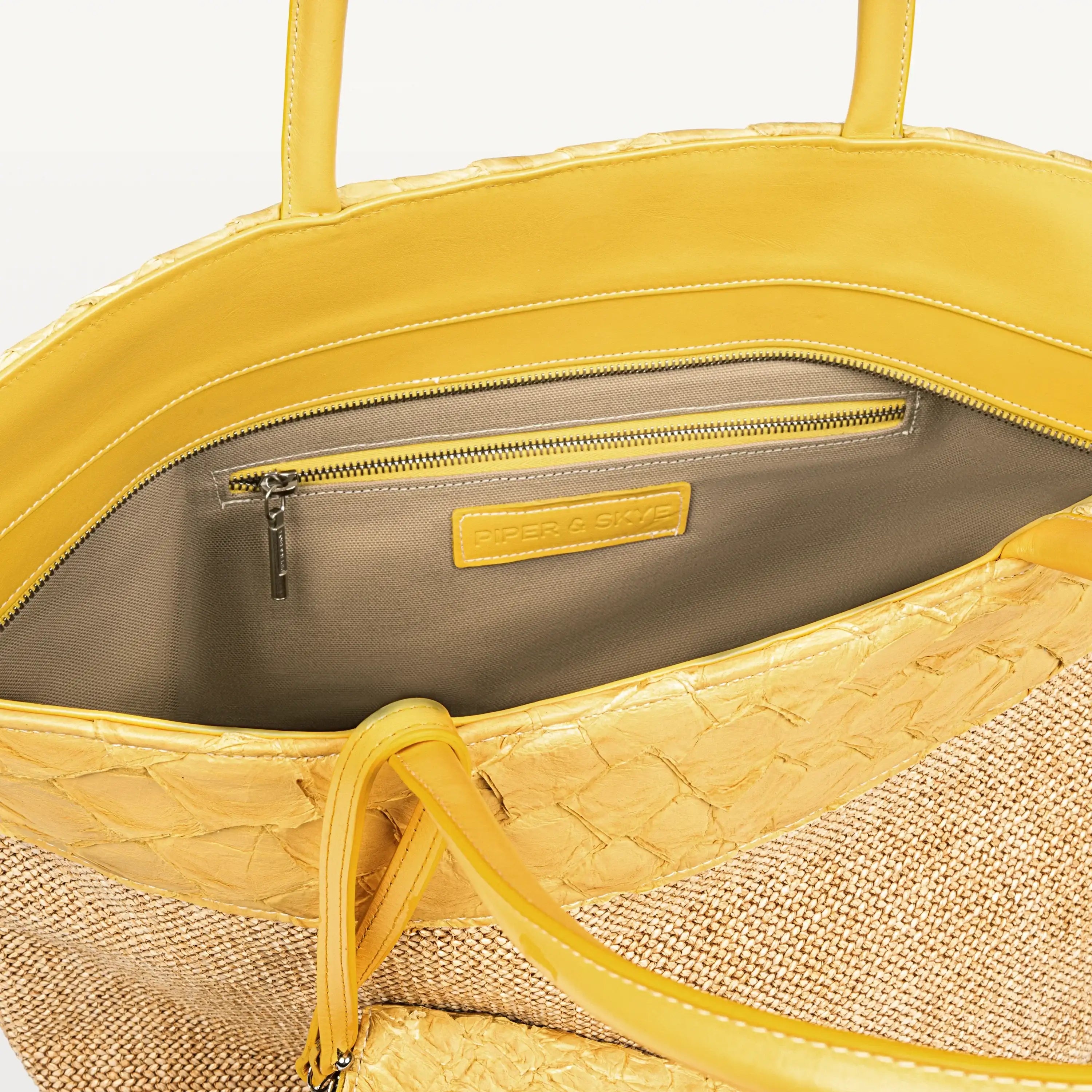 The top zipper of the Rio Beach Bag in honey yellow pirarucu leather is open showing the beige interior lining and inner zipper pocket. 