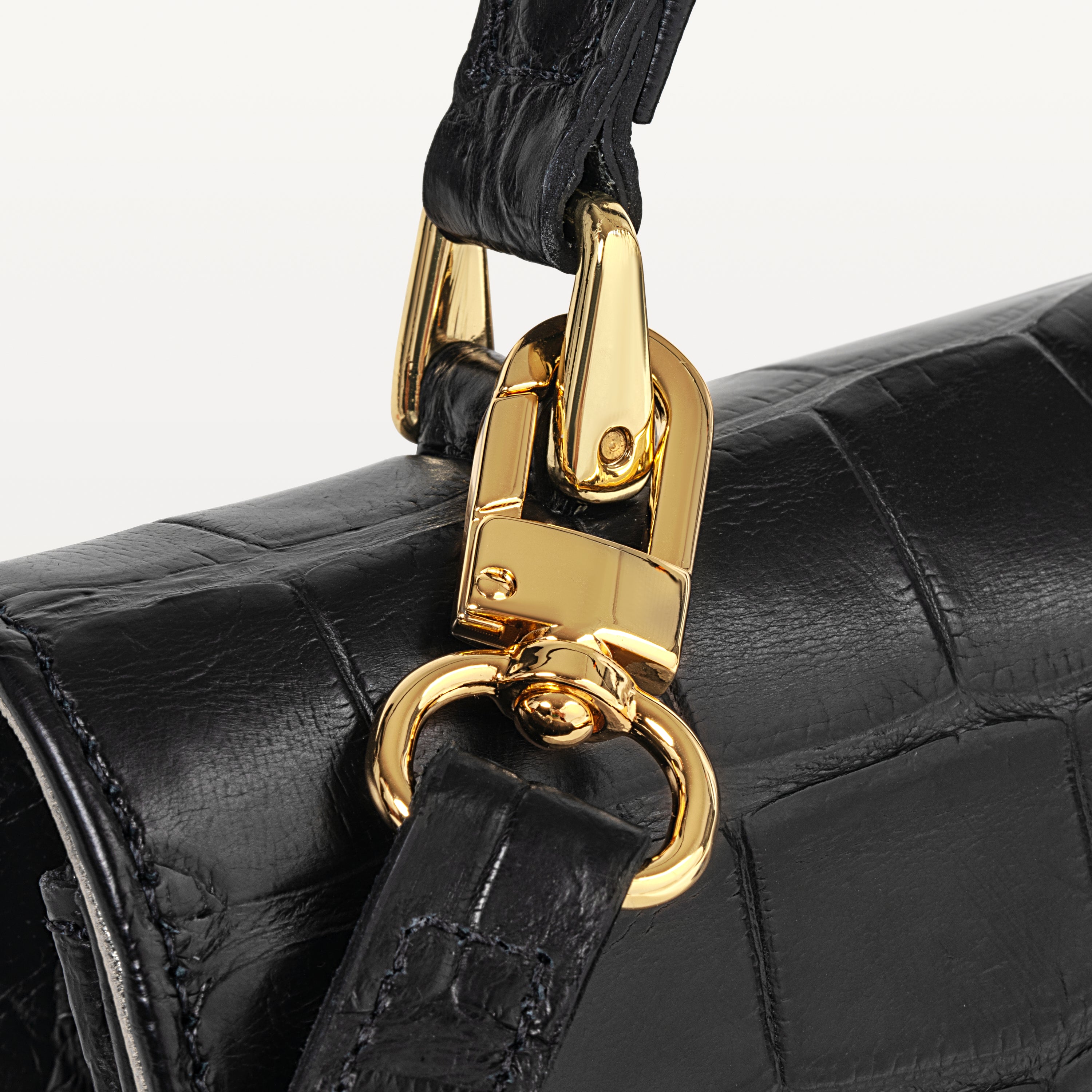 Gold strap hardware of the Soho top handle bag in glossy black alligator leather. 